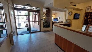 A hotel reception area with a reception desk, a clock, and a framed sign indicating administration hours. - Patagonia Apart Hotel (Puerto Madryn)