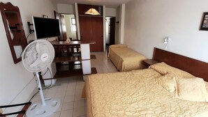 A hotel room with two beds, a desk with a chair, a television, and a standing fan. - Patagonia Apart Hotel (Puerto Madryn)