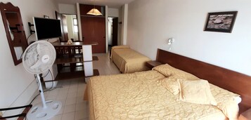 Habitación de hotel con dos camas, un escritorio con silla, un televisor y un ventilador de pie.