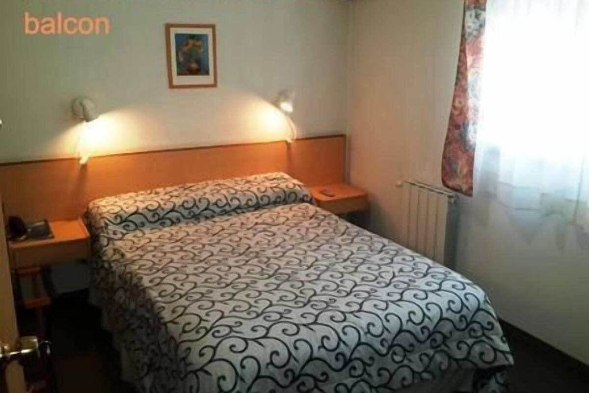 Une chambre pour couples sans balcon, comprenant un lit avec une couvre-lit à motifs, des lampes de chevet et un tableau encadré au mur.