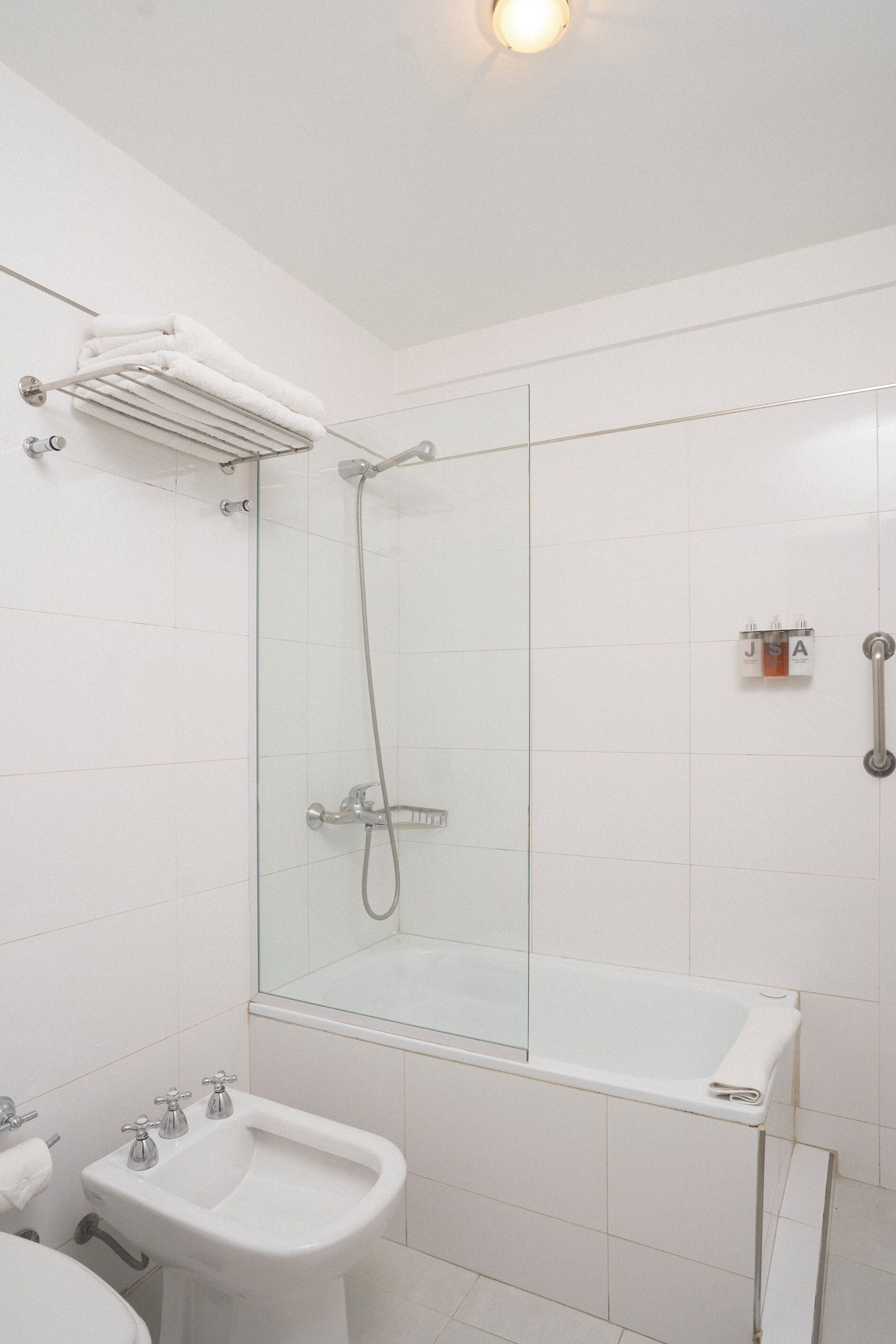 A modern bathroom with a glass-enclosed shower, a white bathtub, a bidet, and a towel rack.