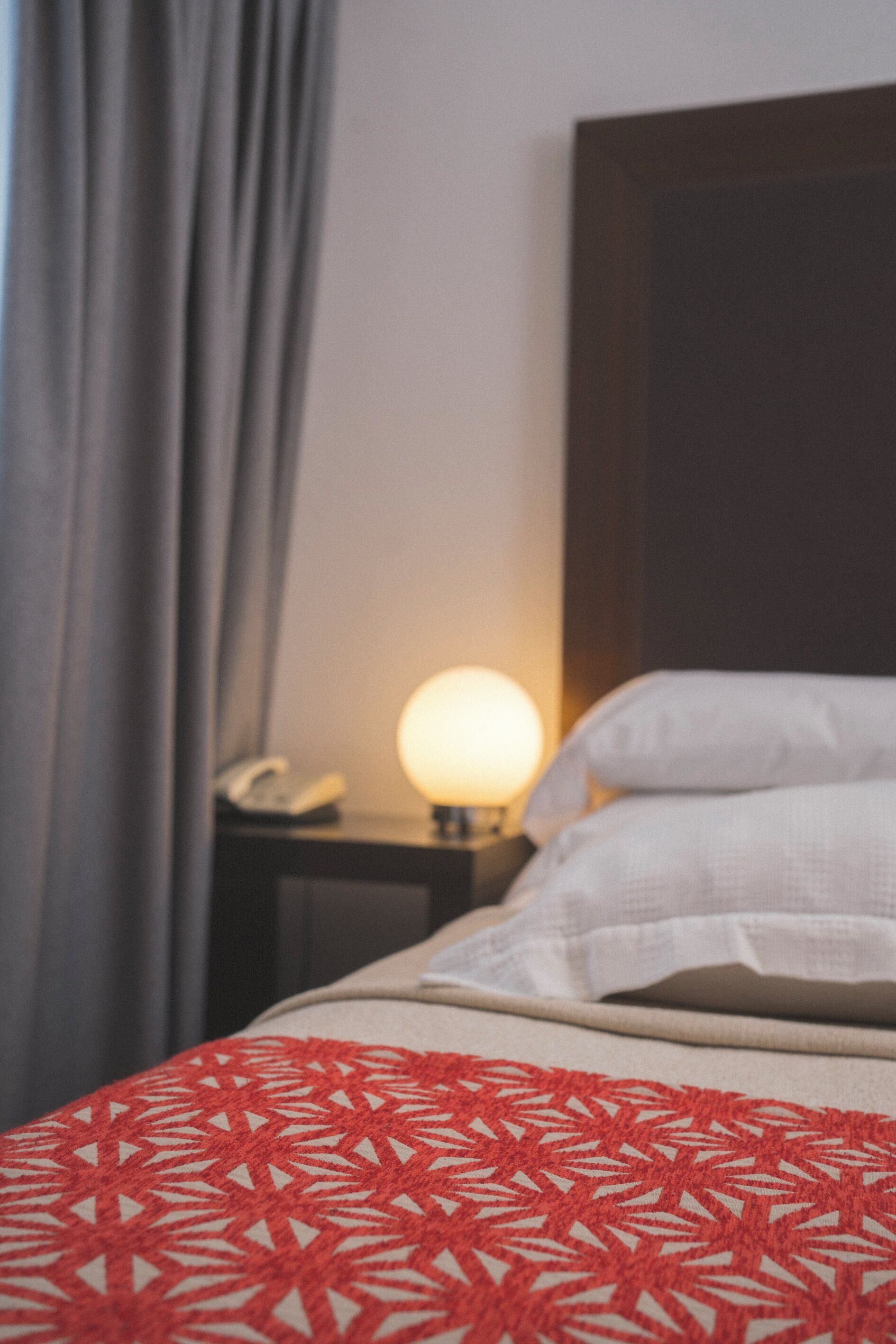 A hotel room with a bed, a bedside lamp, and a telephone on a nightstand.