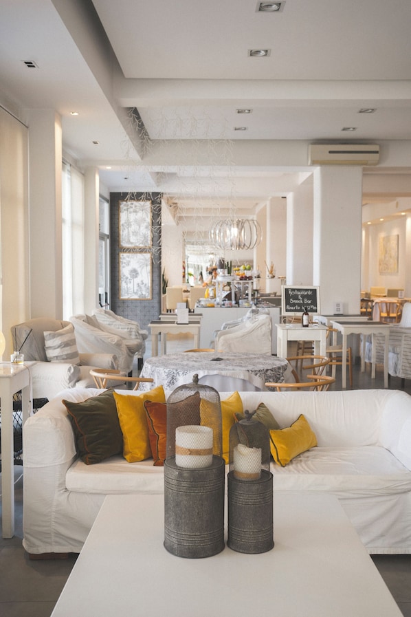 A modern living room with a white sofa, a coffee table with decorative items, and a dining area with a chandelier.