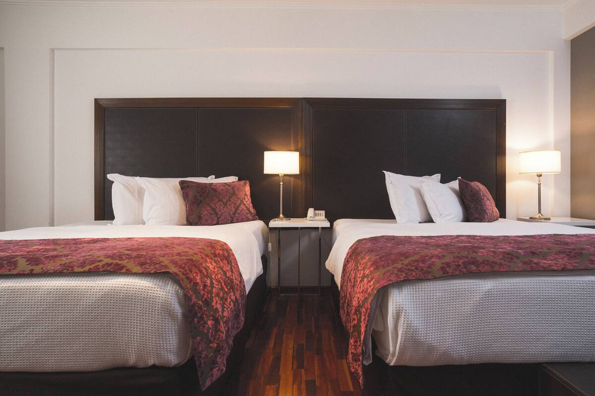 Une chambre d’hôtel avec deux lits, chacun doté d’une tête de lit, de tables de chevet avec des lampes et d’un plancher en bois.