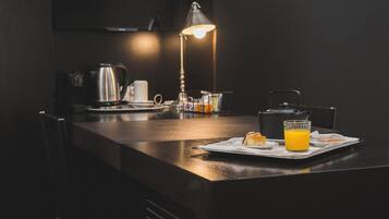 Una cocina moderna con encimera oscura, una tetera, una cafetera, un vaso de jugo de naranja y una lámpara.
