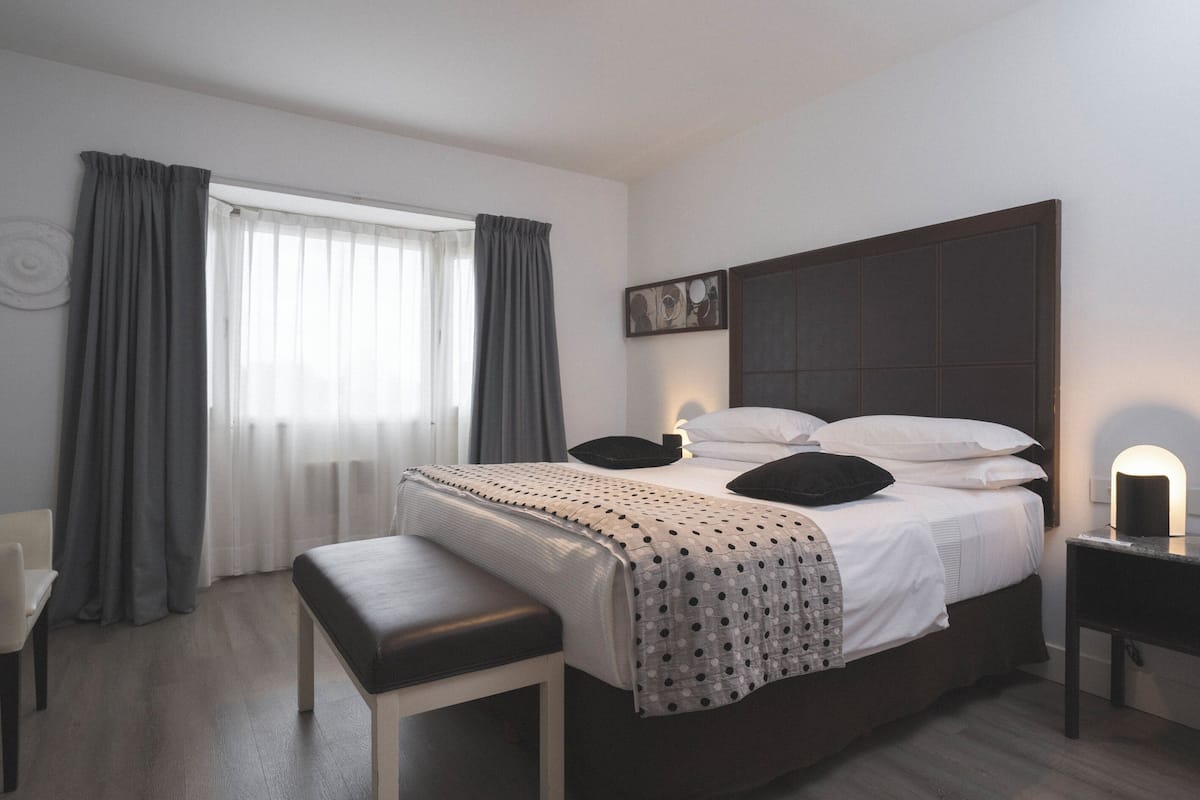 Une chambre à coucher avec un lit, une banquette, une table de chevet et une fenêtre avec des rideaux.