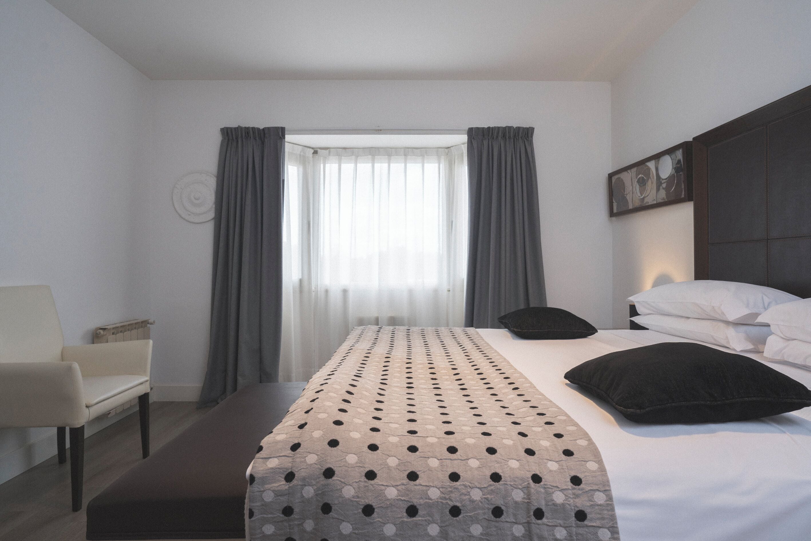 Une chambre d’hôtel moderne avec un grand lit, une table de chevet, une chaise et une fenêtre avec des rideaux.