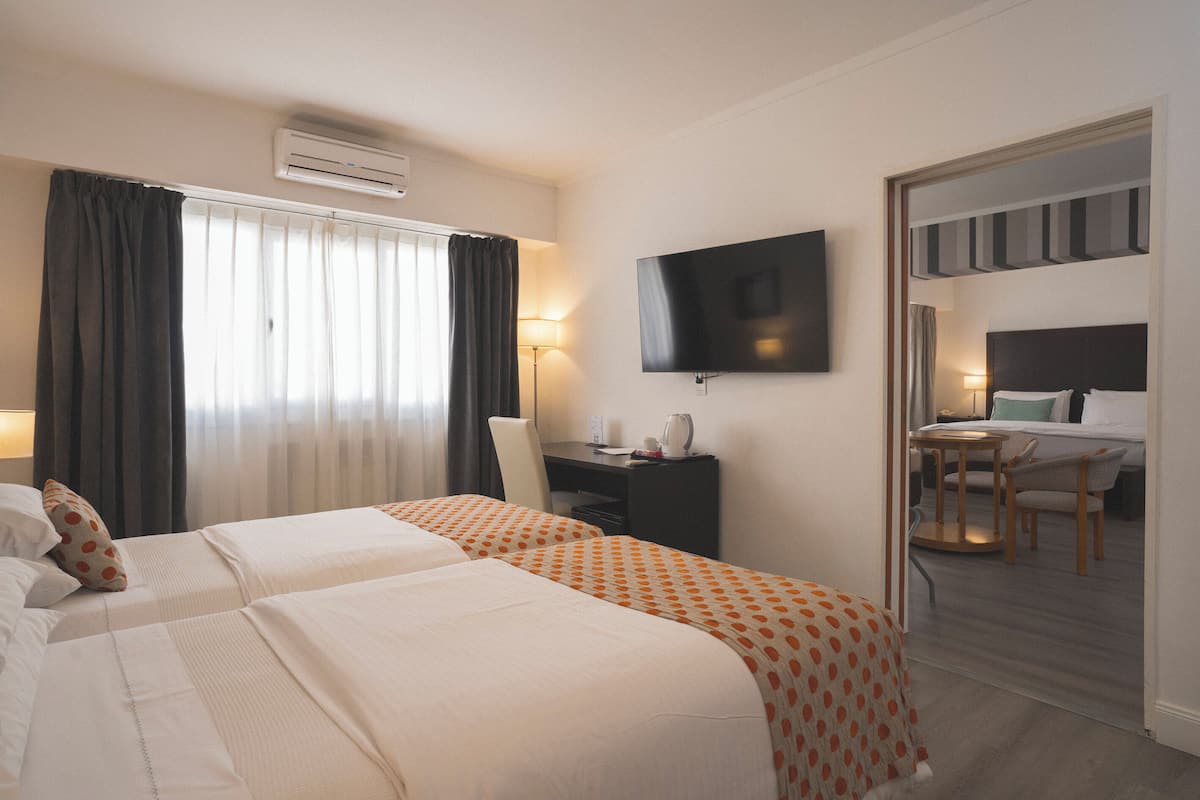 Une chambre d’hôtel avec deux lits, un bureau, une chaise, une télévision et un miroir.