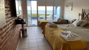 Habitación de hotel con dos camas, una pared de ladrillo, una ventana con vista al mar y un balcón.