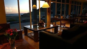 Un salón acogedor con vista al océano, una mesa de centro de madera y un jarrón con flores rojas.
