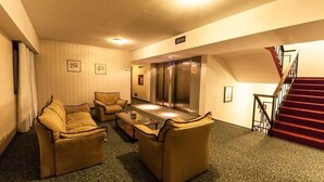 Un vestíbulo de hotel con zona de estar, mostrador de recepción, ascensor y escalera.