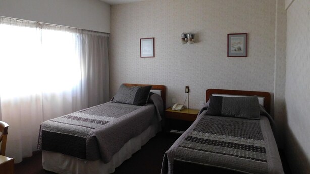 Habitación de hotel con dos camas individuales, una mesita, una silla y una ventana con cortinas.