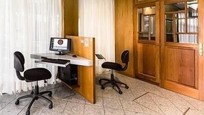 Una habitación con un escritorio de madera, dos sillas de oficina negras, una computadora y una puerta de madera con paneles de vidrio.