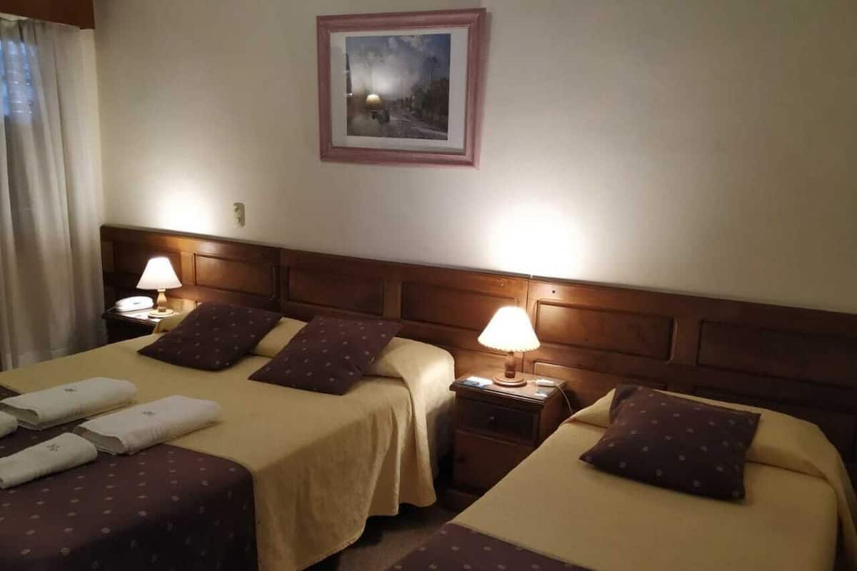 Ett hotellrum med två sängar, var och en med en kudde och en lampa. På väggen ovanför sängarna hänger en inramad tavla.