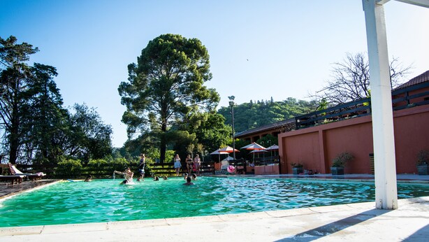 A swimming pool with people, surrounded by trees and a building with outdoor seating. - San Pedro Hotel (Rio Ceballos)