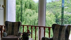 A room with two upholstered chairs, a small round table, and a view of lush greenery through large windows. - San Pedro Hotel (Rio Ceballos)