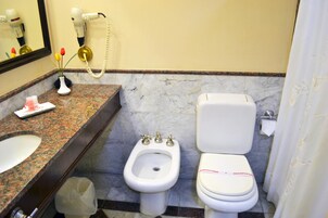 Un baño con lavamanos de mármol, bidé, inodoro y un secador de pelo en la pared.