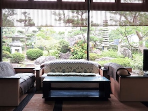 A room with a bed, two chairs, a small table, and a view of a garden with rocks and a pagoda. - Yumeya Hanatsukushi (Awara)