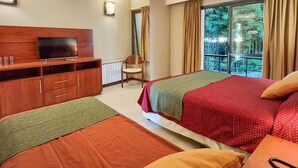 Habitación de hotel con dos camas, televisión, silla y ventana con vistas a zonas verdes.