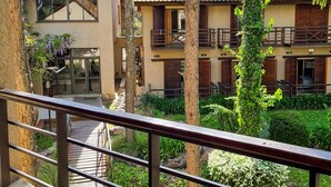 Un patio con un edificio que tiene balcones, una escalera de piedra y abundante vegetación.