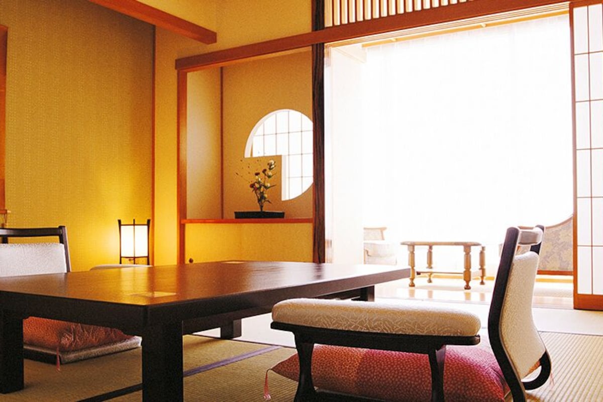 A traditional Japanese room with tatami flooring, a low table, and two chairs.