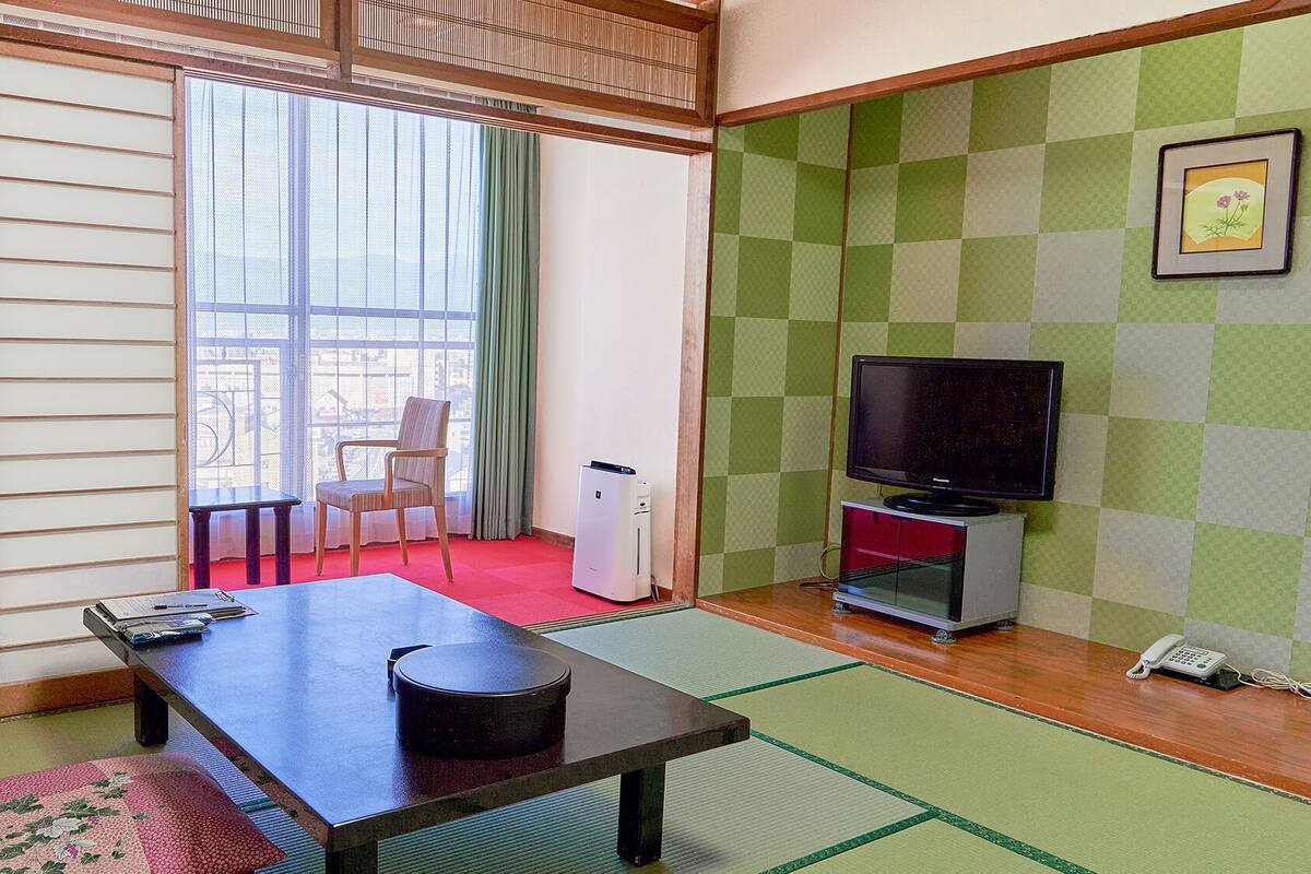 A traditional Japanese room with tatami flooring, a sliding door, a television, and a small table.