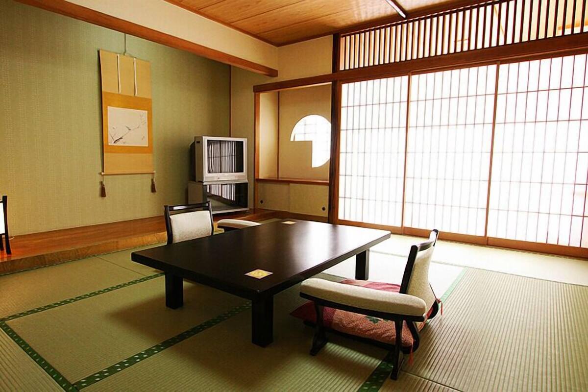A traditional Japanese room with tatami flooring, a low table, a television, and sliding doors.