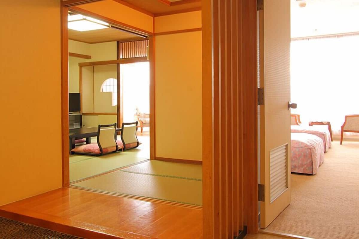 A traditional Japanese room with tatami flooring, a sliding door, a bed with pink bedding, and a small table with chairs.