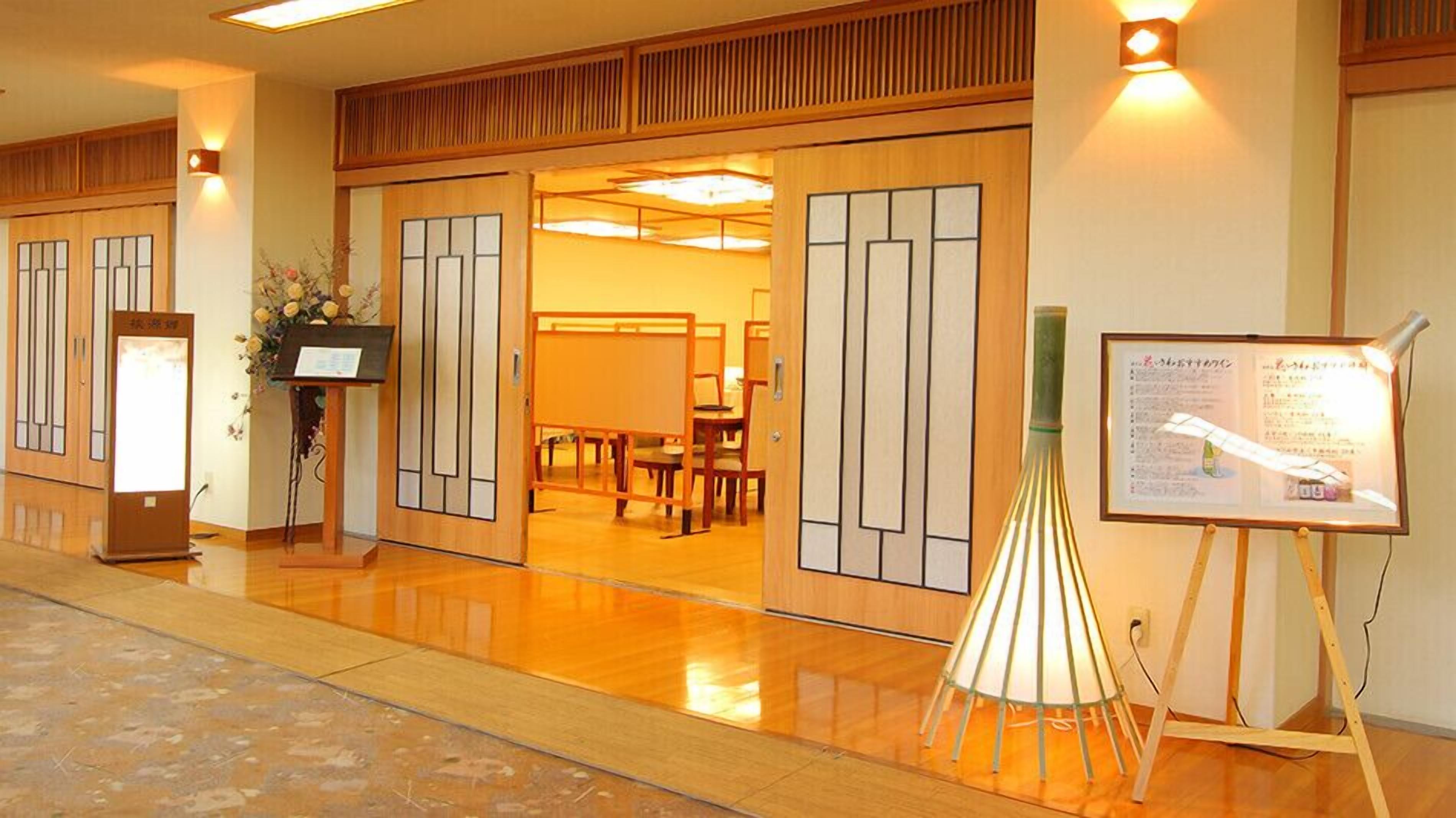 A traditional Japanese room with sliding doors, a reception desk, a digital information board, and a small table with a lamp.