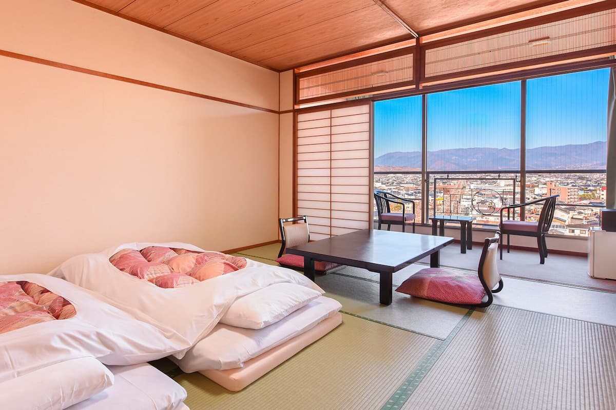 A room with two beds, a table, chairs, and a view of a cityscape through large windows.