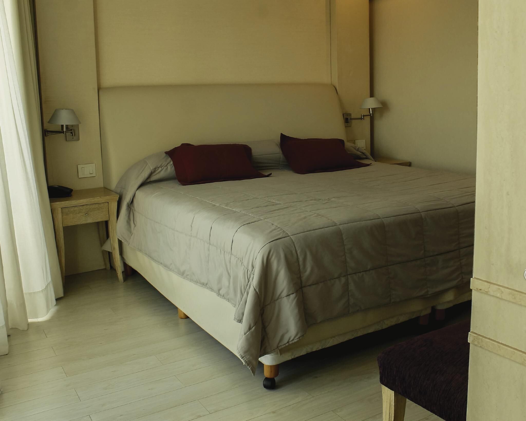 A neatly made bed with a beige duvet, two pillows, and a wooden nightstand with a lamp.