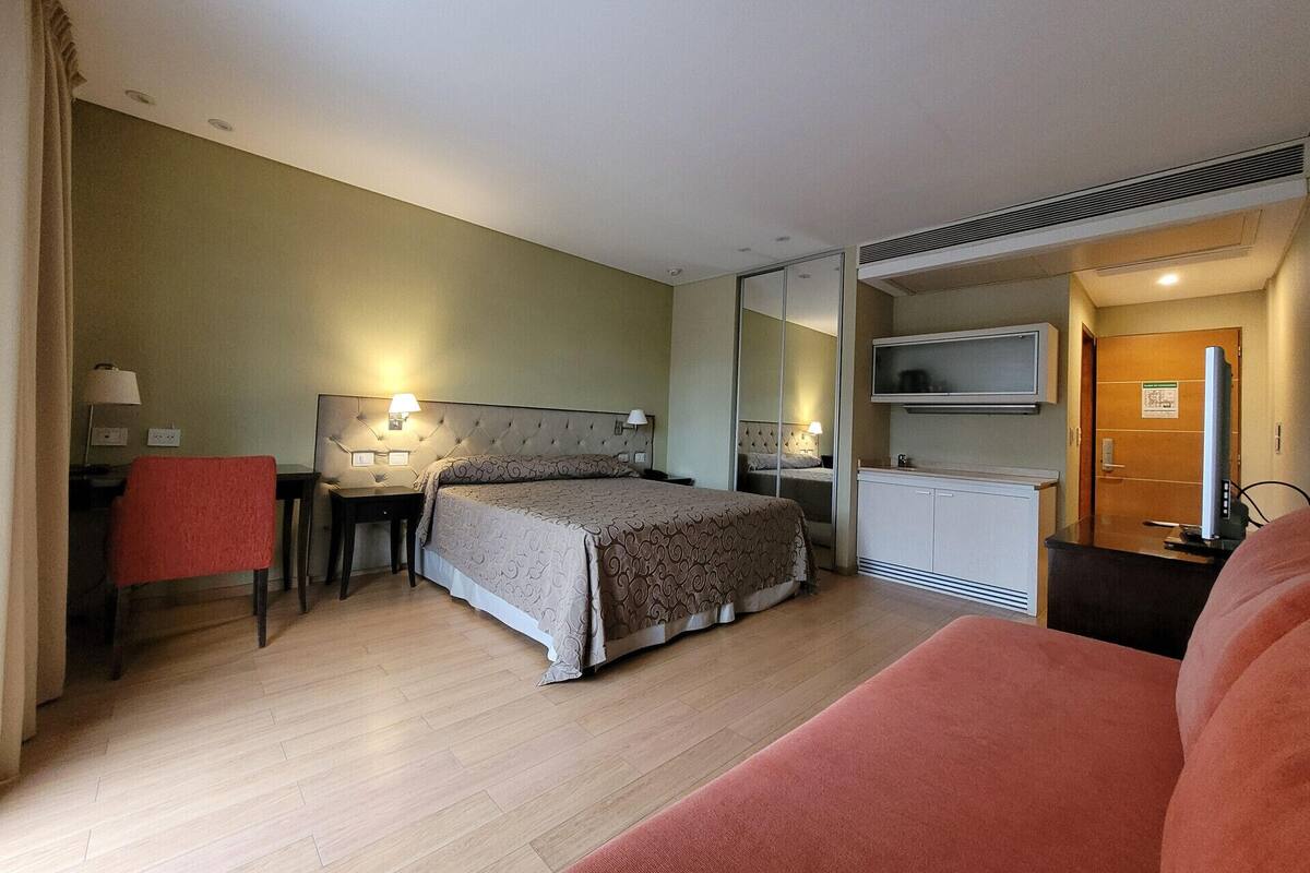 Una habitación de hotel con cama, escritorio, silla, televisor y armario.