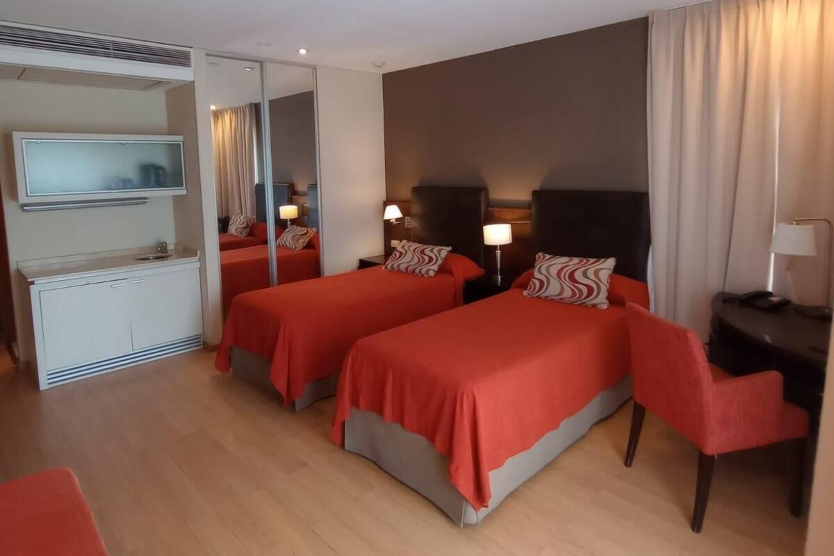 Habitación de hotel con dos camas, un escritorio, una silla, un televisor y un espejo.
