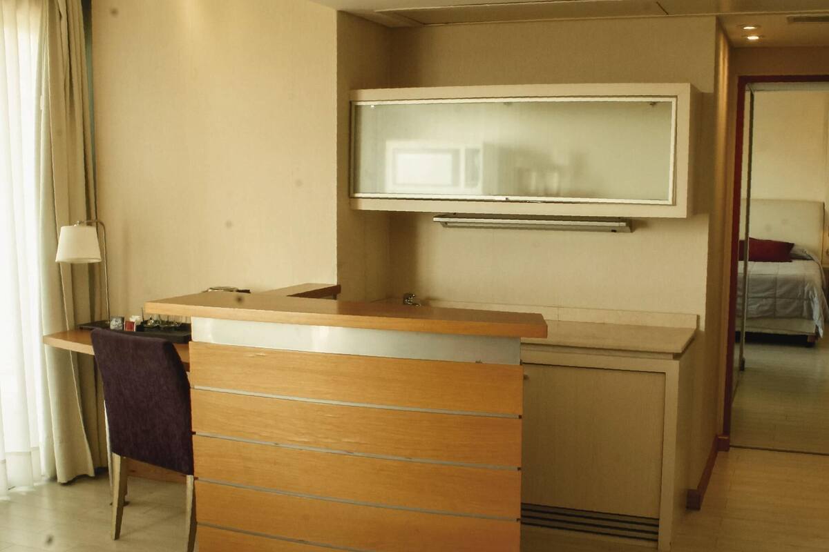 Habitación de hotel con un escritorio de madera, un televisor de pantalla plana montado encima y una cama al fondo.