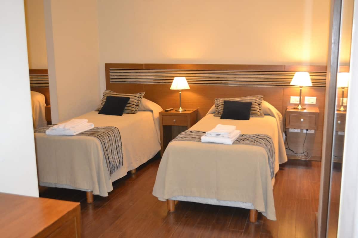 Habitación de hotel con dos camas, cada una con cabecera, mesitas de noche, lámparas y toallas dobladas con cuidado.