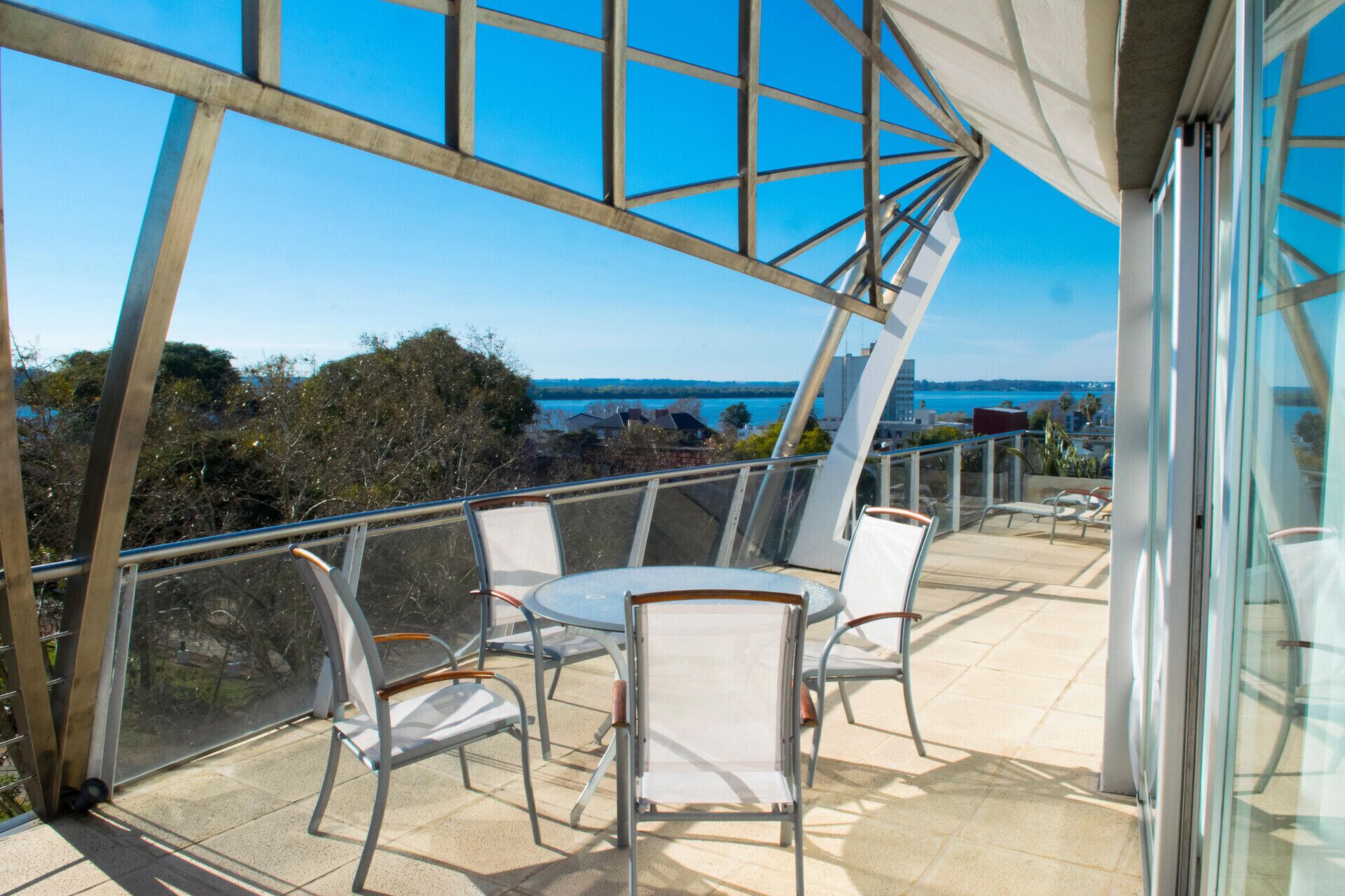 A balcony with a glass railing, a table, and four chairs.