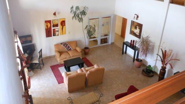 A spacious living area with a sofa set, a coffee table, and a dining table. There are potted plants and artwork on the walls. - Piedras del Lago Hotel (Federaciän)