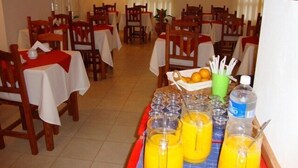 A dining area with tables set for breakfast, including juice and a basket of oranges. - Piedras del Lago Hotel (Federaciän)