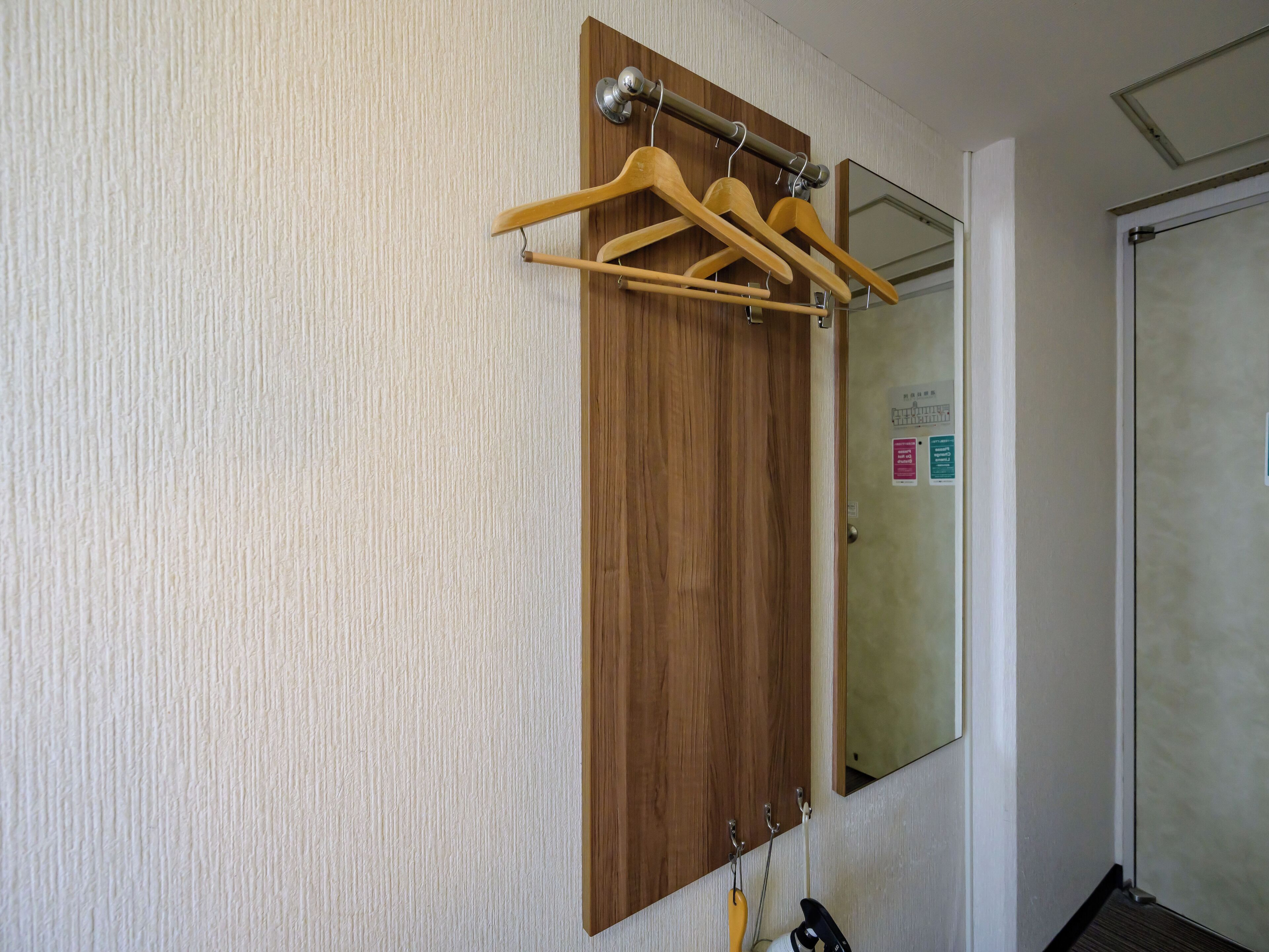 Un armario de madera con un espejo encima, un perchero con perchas de madera y una puerta con manija.