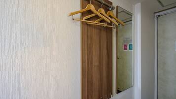Un armario de madera con un espejo encima, un perchero con perchas de madera y una puerta con manija.