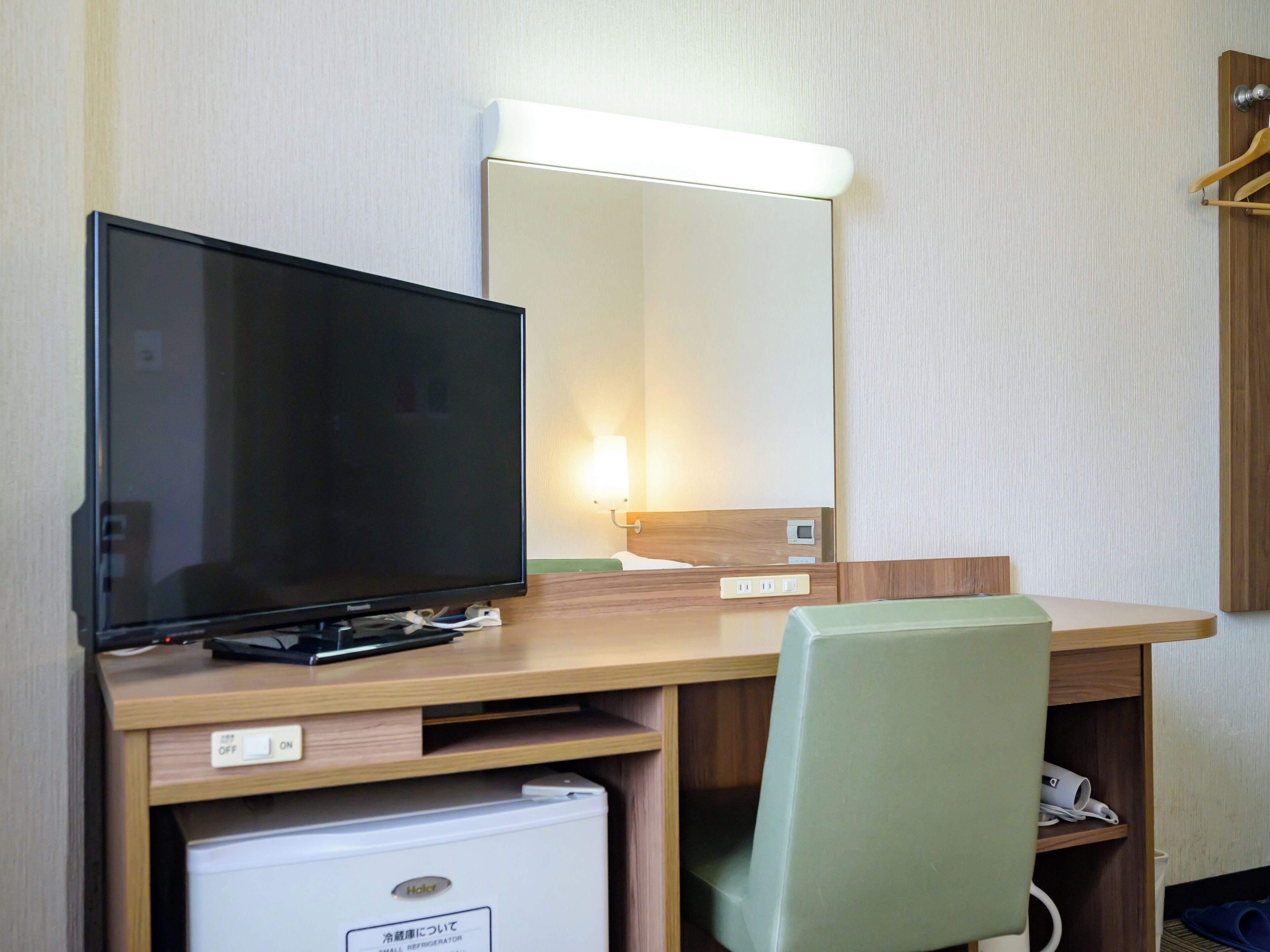 Quarto de hotel com escrivaninha de madeira, televisão, espelho e um pequeno frigorífico.