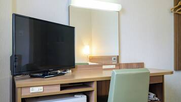 Quarto de hotel com escrivaninha de madeira, televisão, espelho e um pequeno frigorífico.