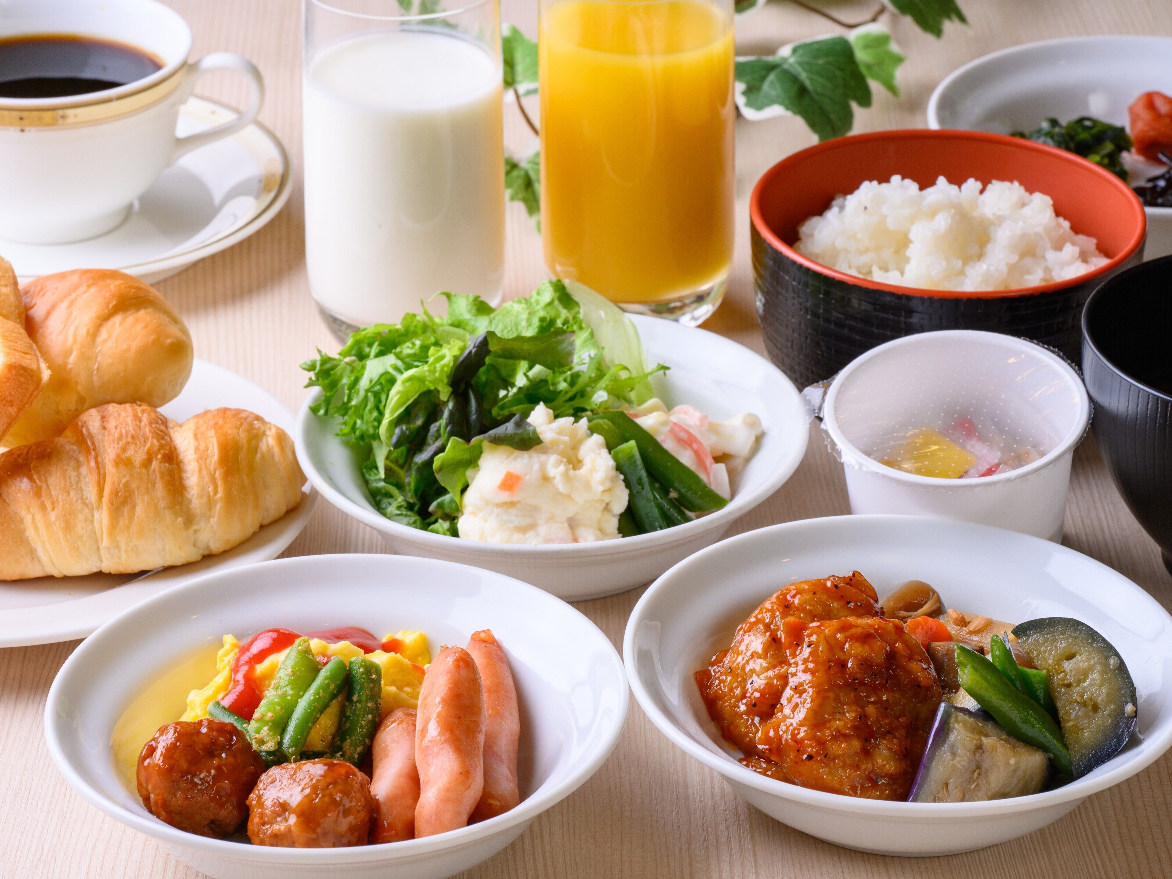 A table with various dishes including croissants, a salad, rice, and meatballs.