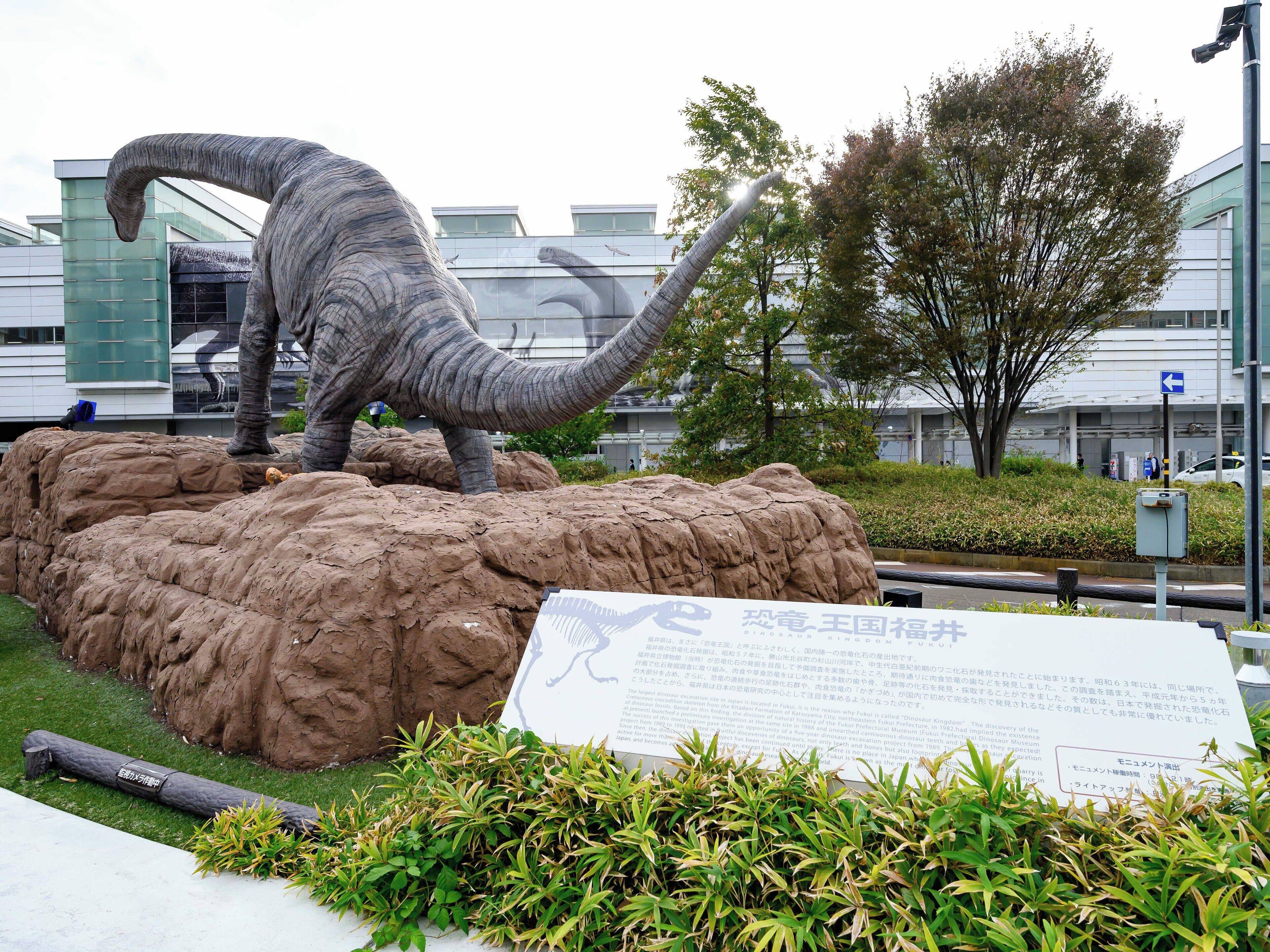 A dinosaur statue on a rocky base with a sign in front.