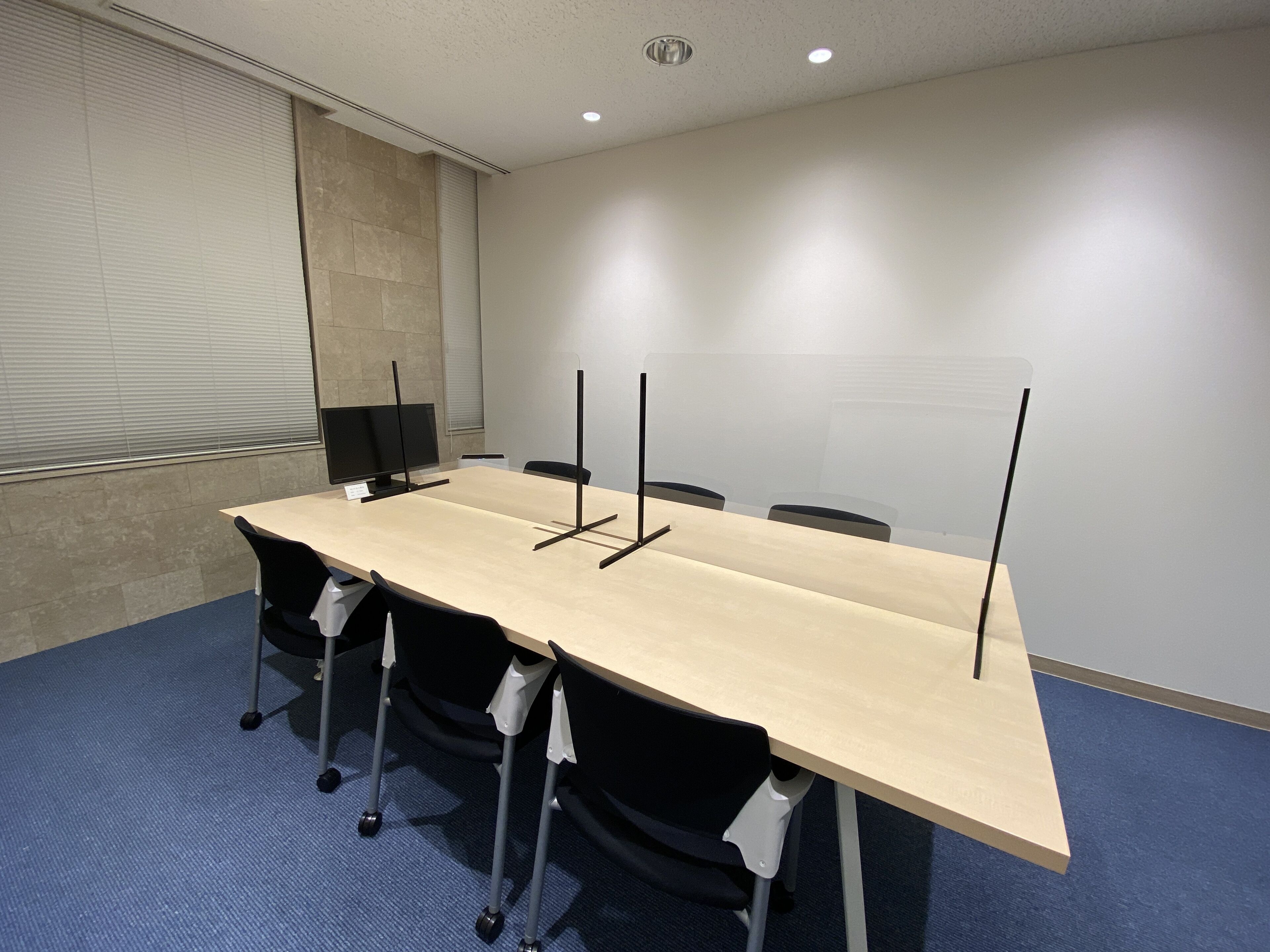 A conference room with a long table, four chairs, two monitors, and a whiteboard.