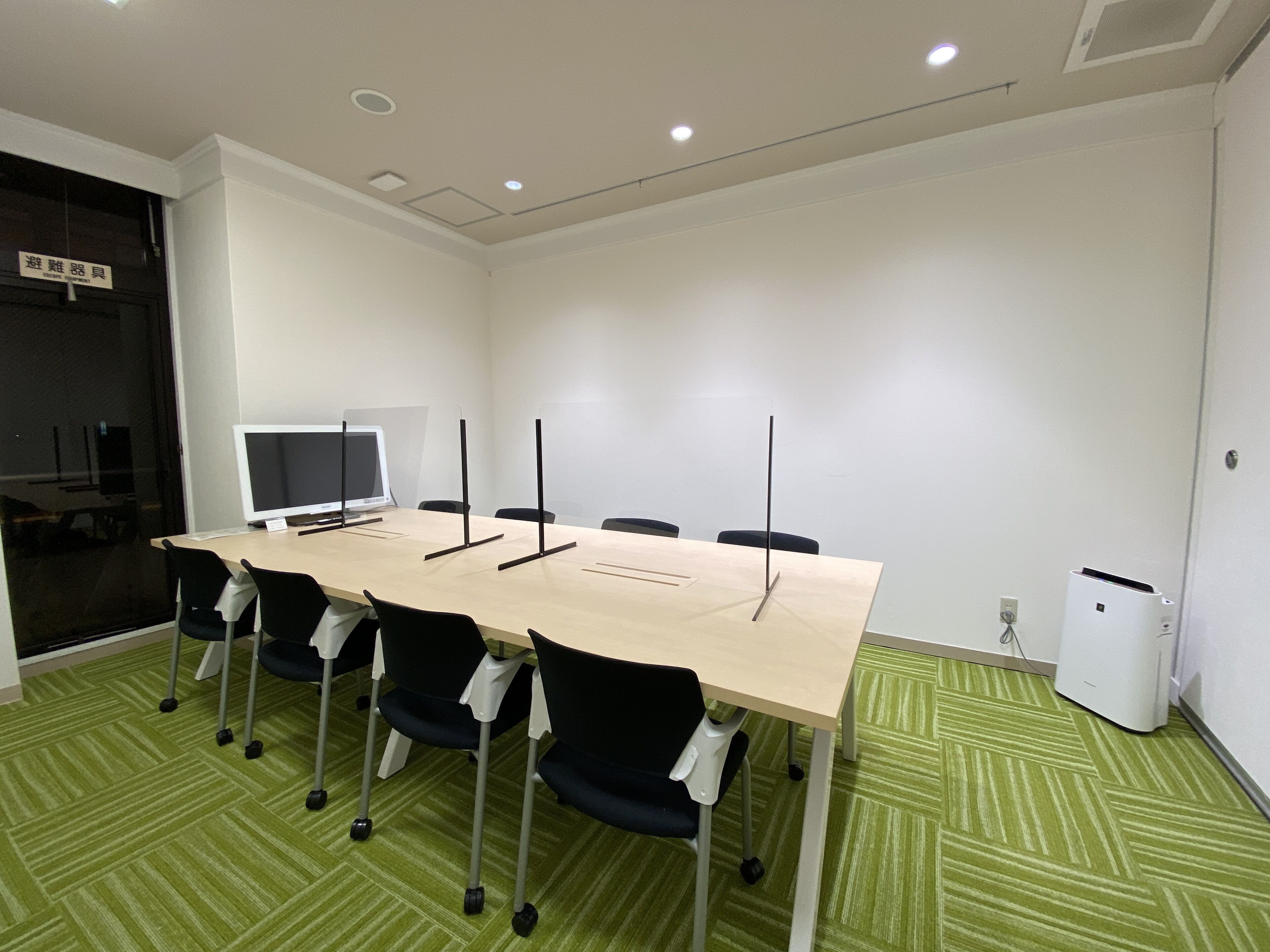 Un salón de conferencias con una larga mesa, seis sillas, un monitor de computadora y una pizarra.
