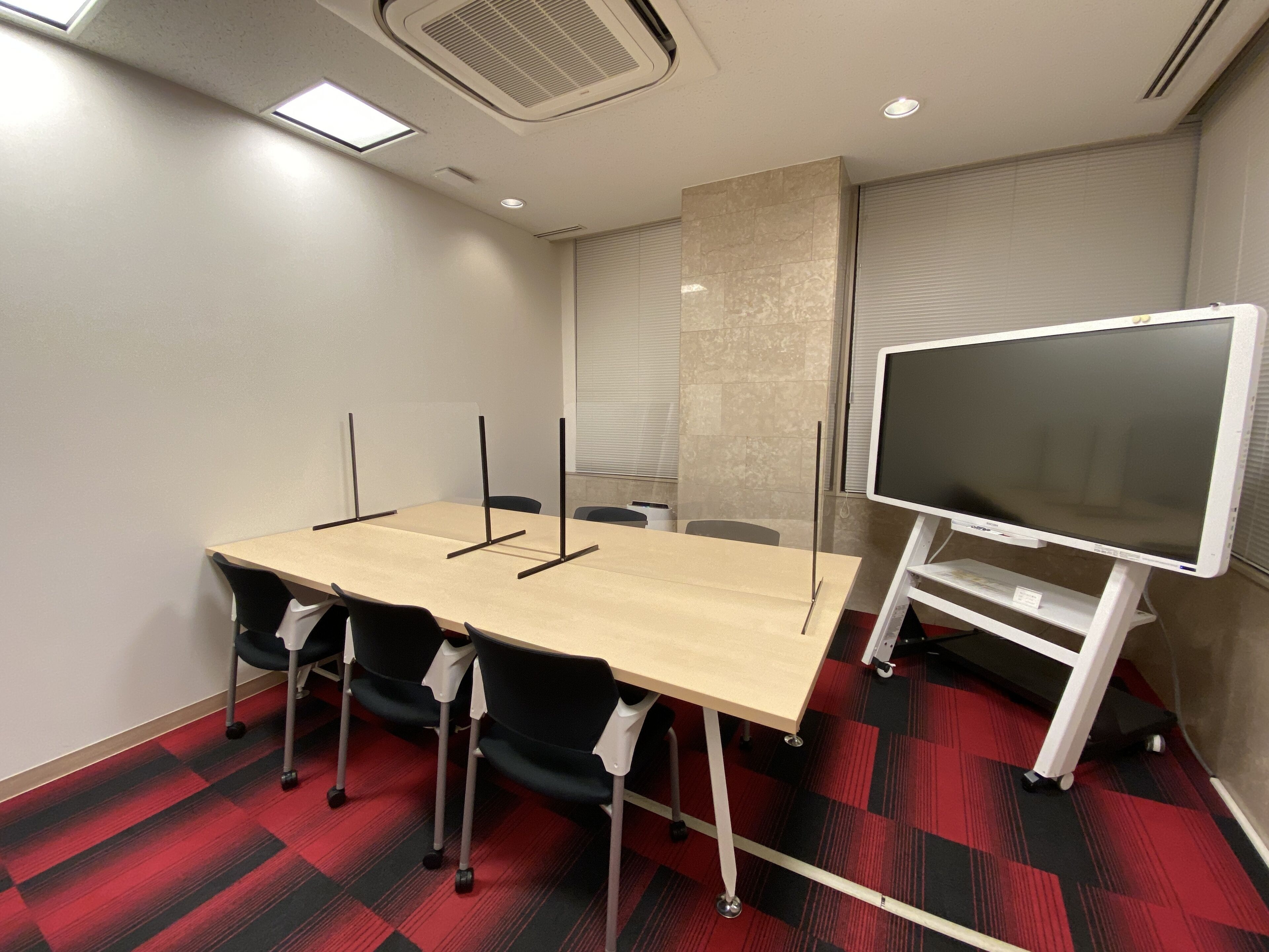 Un salón de conferencias con una gran mesa, sillas, una pizarra y una pantalla de proyector.