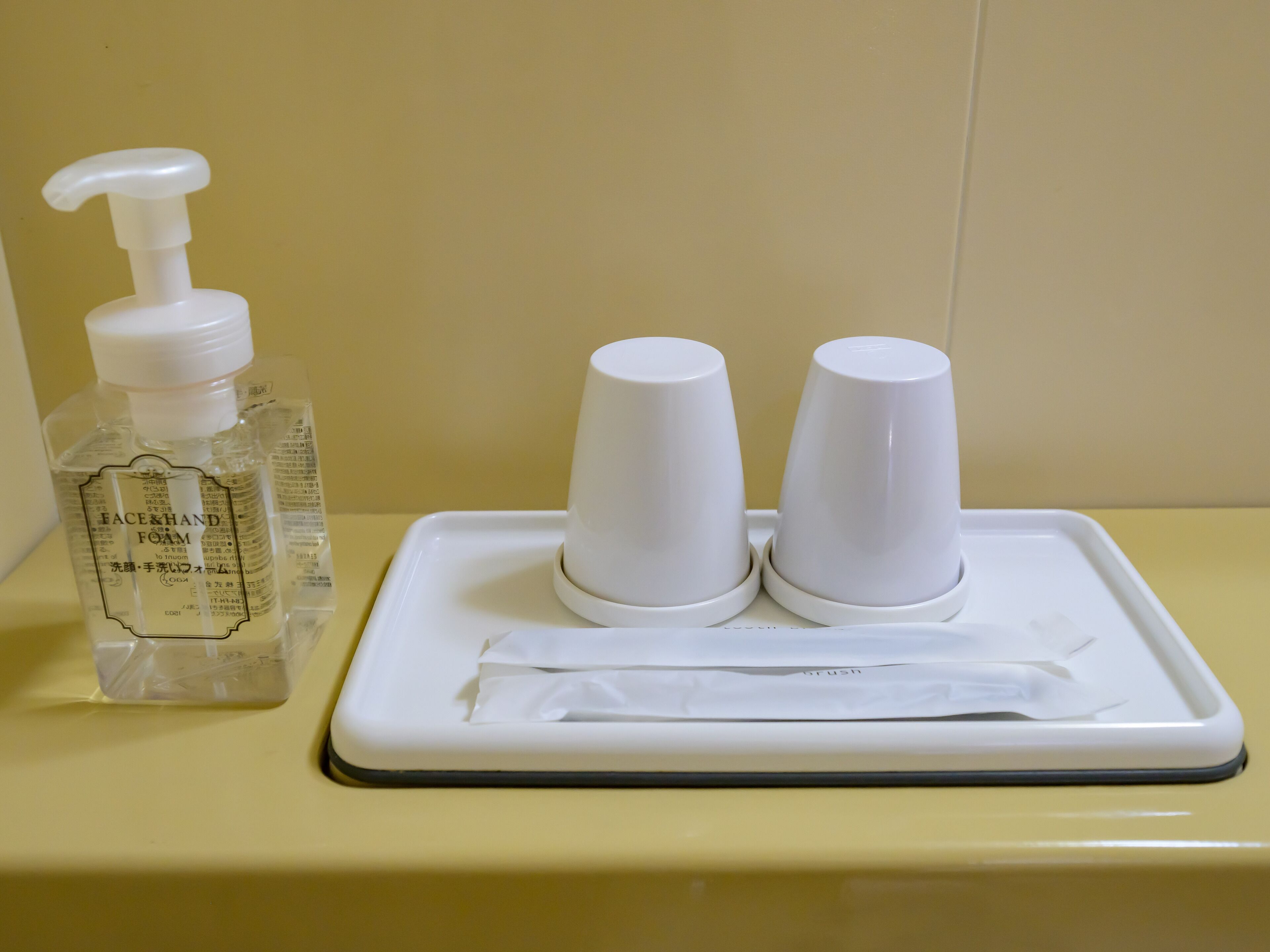 A bathroom sink with a bottle of hand soap and two paper cups on a tray.