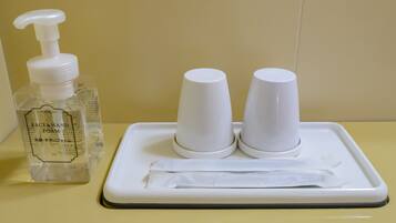 A bathroom sink with a bottle of hand soap and two paper cups on a tray.