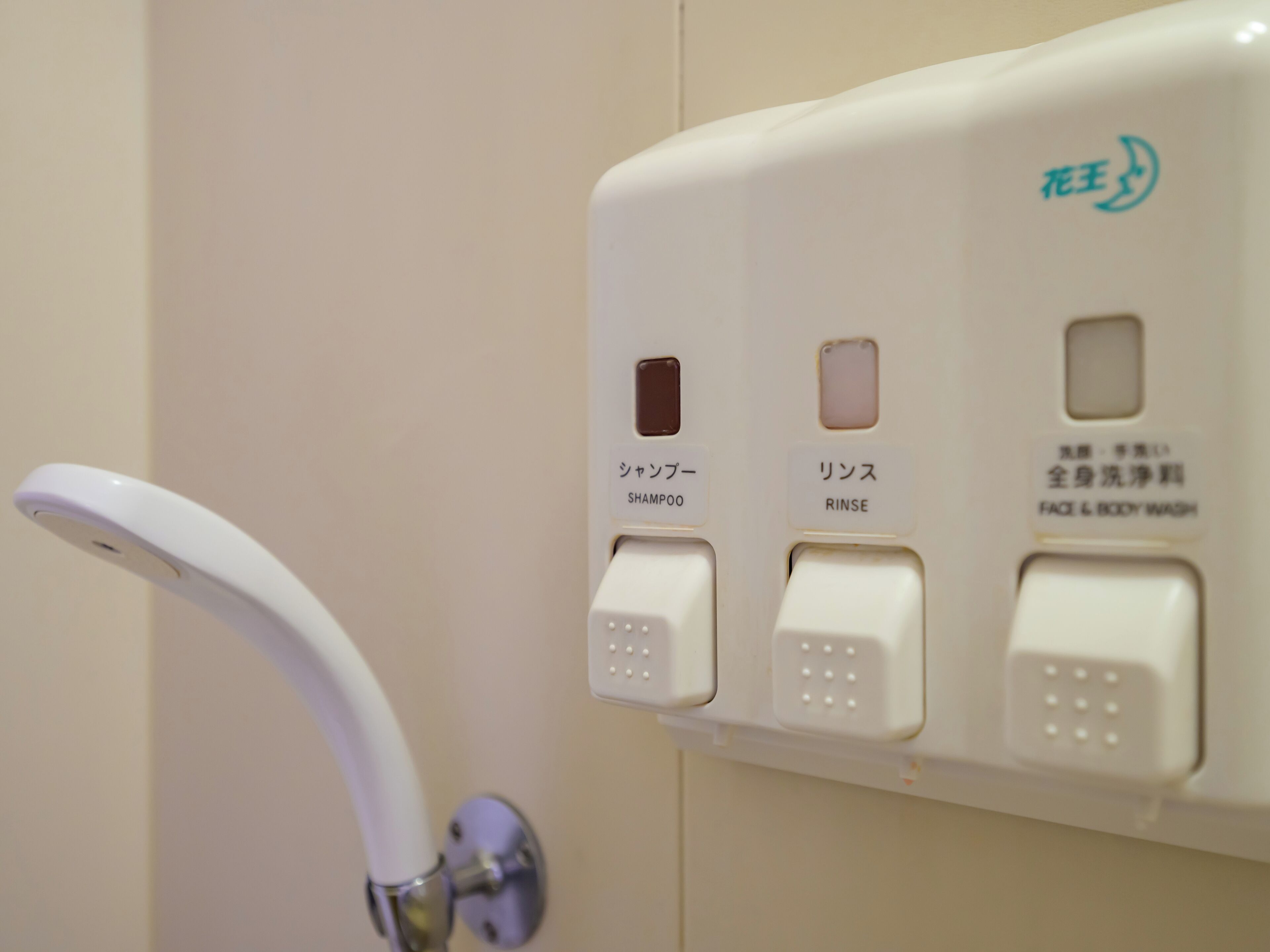 A bathroom with a white faucet and three buttons labeled for shampoo, rinse, and face & body wash.